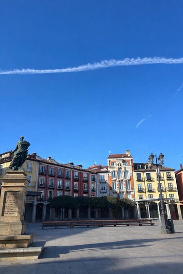 A plaza with colorful buildings, a statue, and a clear sky with contrails. 1