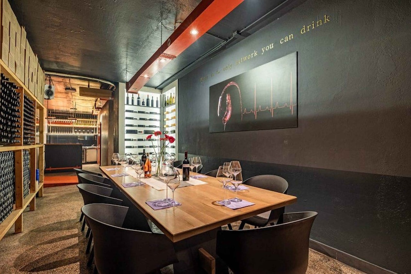 A wine tasting room with a long wooden table set for six, wine bottles on shelves, and a wall with a heartbeat graphic. 1
