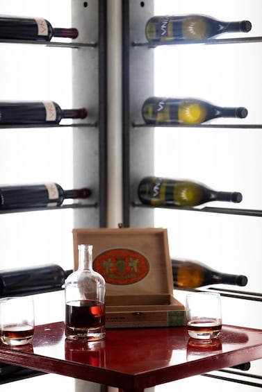 A wine rack with bottles, a wooden box, and two glasses on a table. 2
