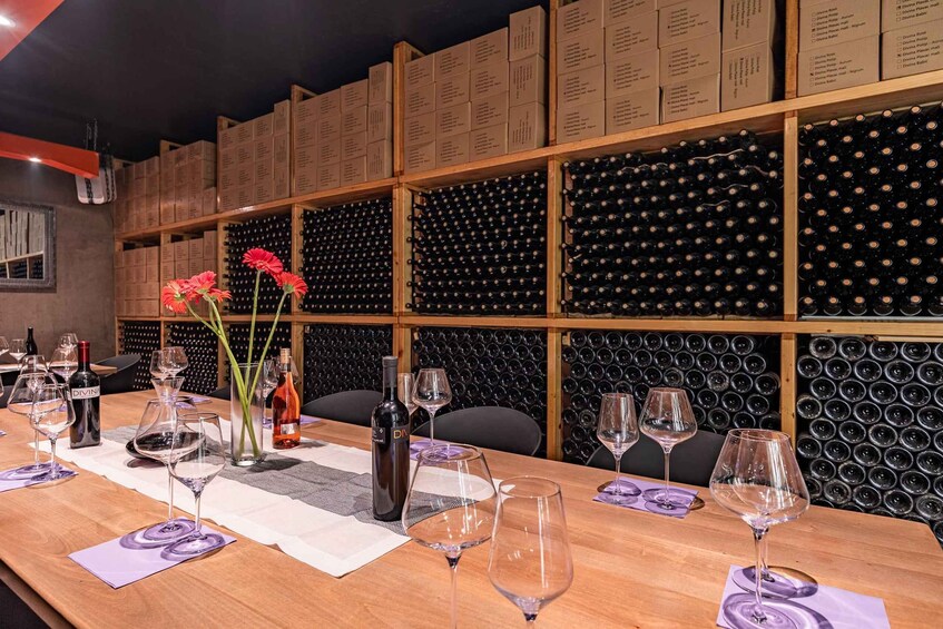 A wine tasting room with wooden shelves, wine bottles, and glasses on a table. 3