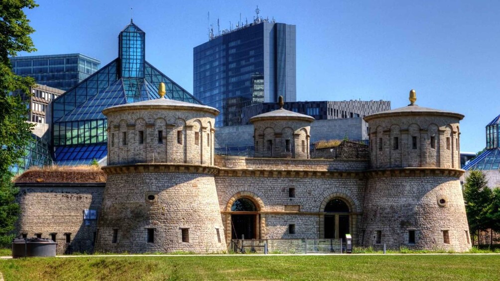 A historic stone building with two domed towers, surrounded by modern skyscrapers. 1