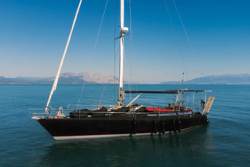 A black sailboat with white trim anchored in calm waters, with mountains in the background. 3