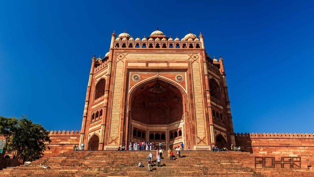 A large, ornate red sandstone gateway with intricate carvings and domes, surrounded by a low wall and steps leading up to it. 2