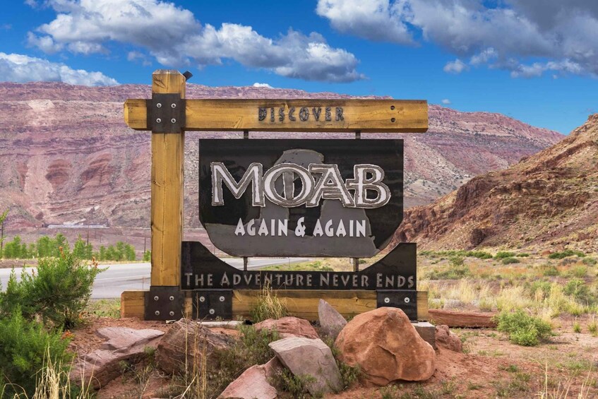 A wooden sign with 'MOAB' and 'DISCOVER' on it, set against a mountainous backdrop. 3