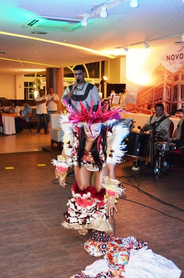 A person in a colorful costume with feathers and beads, standing on a stage with a microphone. 4
