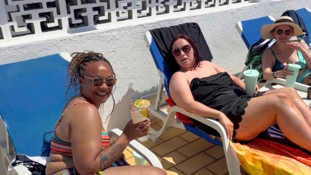 Two people relaxing on sun loungers by a pool with a geometric wall pattern in the background. 2