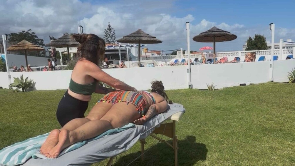 A person receiving a back massage on a beach with umbrellas and people in the background. 1