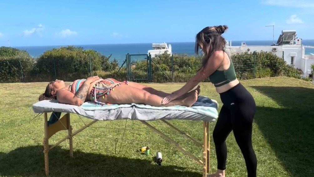 A person lying on a massage table outdoors with a view of the ocean and buildings in the background. 4