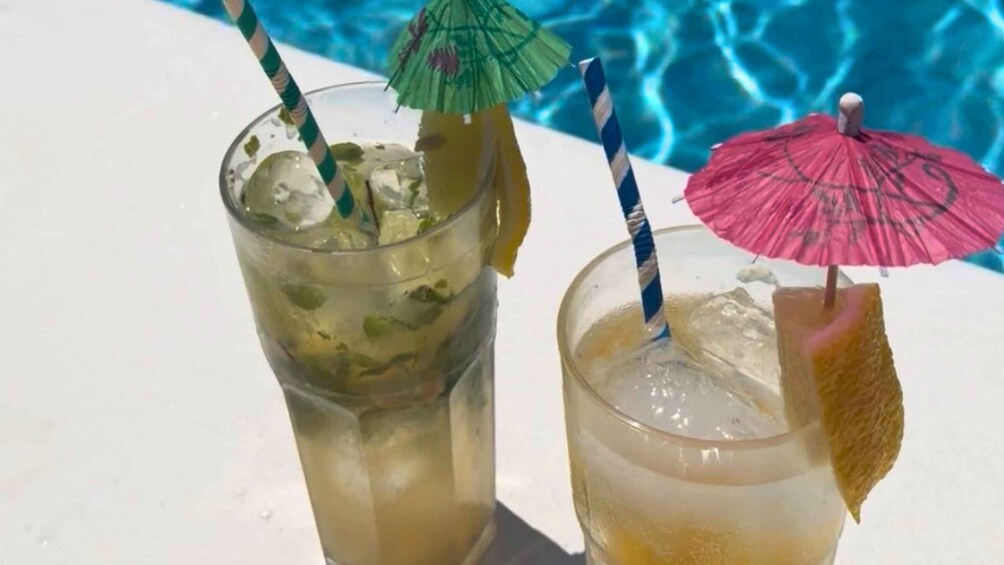 Two drinks with umbrellas and straws by a pool. 3