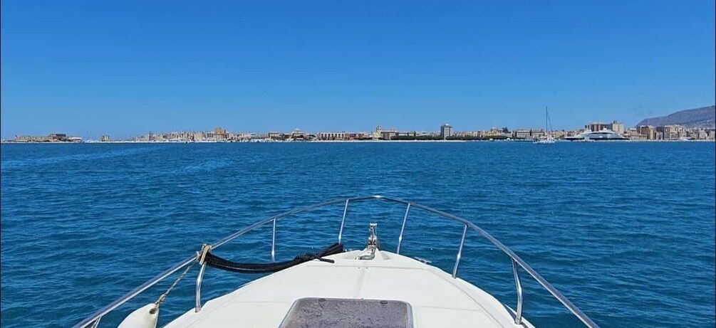 A boat on calm blue waters with a city skyline in the distance. 1