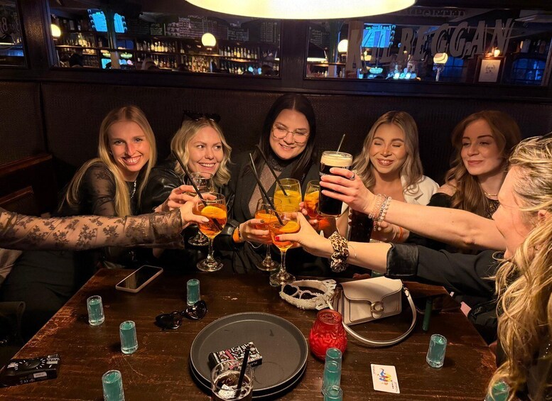 A group of people toasting with drinks at a bar with a neon sign in the background. 5