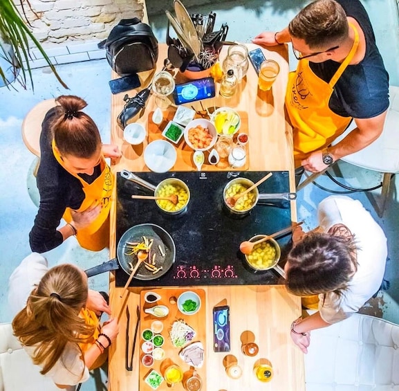 A group of people cooking outdoors with various ingredients and cooking utensils on a wooden table. 4
