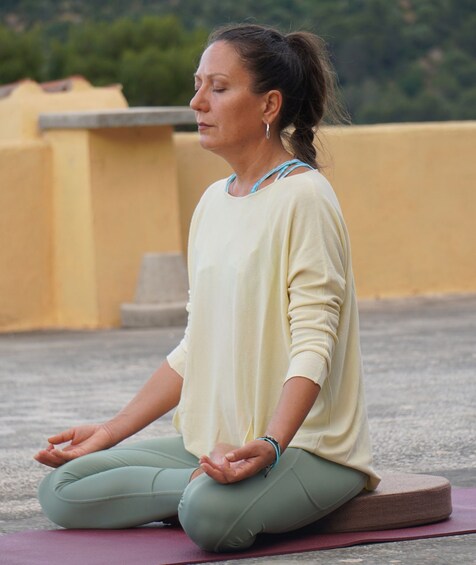 A person sitting cross-legged on a mat outdoors. 4