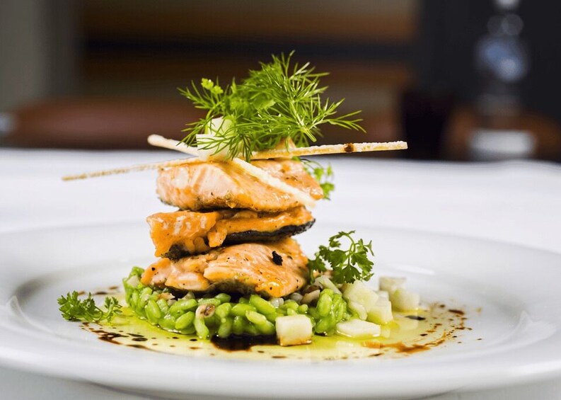 A stack of salmon fillets on a plate with green garnish and sauce. 3