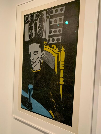 A framed artwork with a figure seated at a table, a chair with a decorative backrest, and a wall with circular patterns. 5