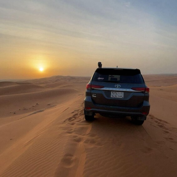A vehicle parked on a desert sand dune with a sunset in the background. 4