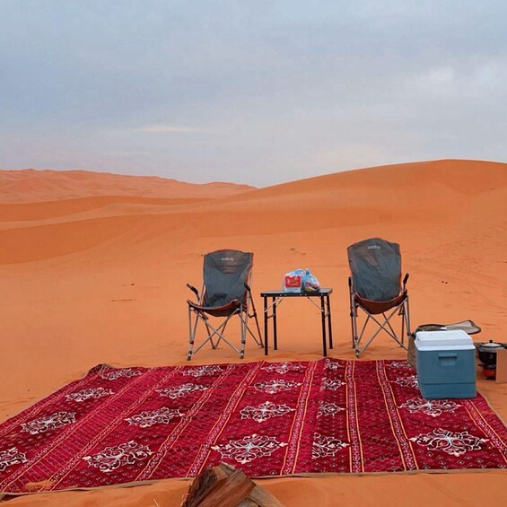 A desert with two chairs and a table set up on a red patterned rug. 2