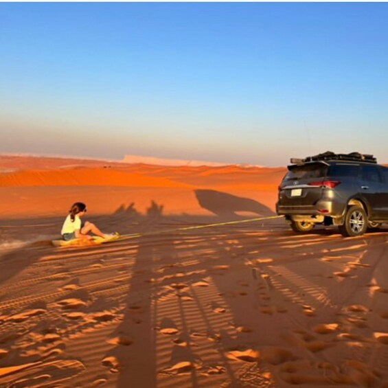 A desert landscape with a person sitting on the sand and a vehicle parked nearby. 3