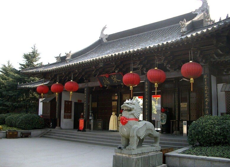 A traditional Chinese building with ornate roof tiles, red lanterns, and a stone lion statue in front. 1