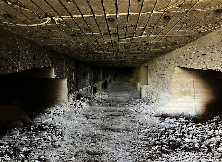A dimly lit, abandoned tunnel with concrete walls and a rough, rocky floor. 5