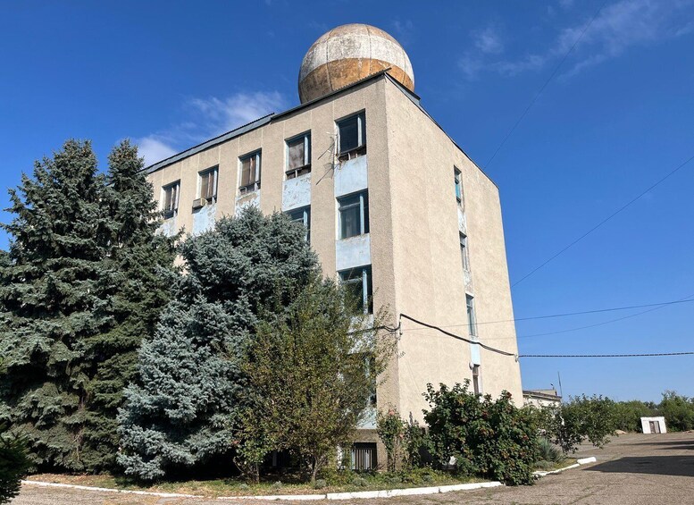 A large, multi-story building with a rounded dome on top, surrounded by trees and shrubs. 4