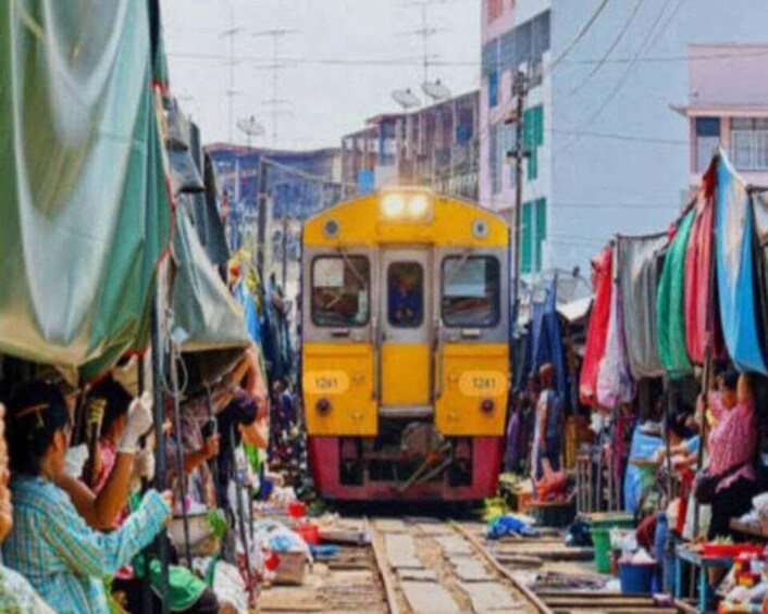 A yellow train on tracks in a market area with stalls and people. 1