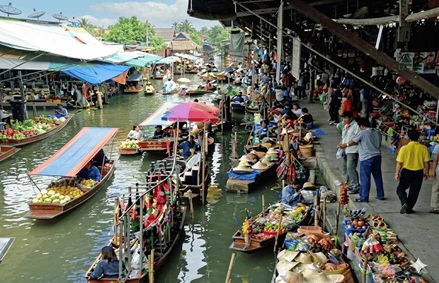 A bustling floating market with canoes loaded with goods, vendors on the shore, and a river setting. 5