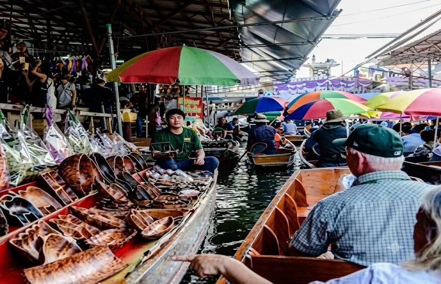 A crowded waterway with boats carrying goods, under colorful umbrellas, and a covered market area in the background. 4