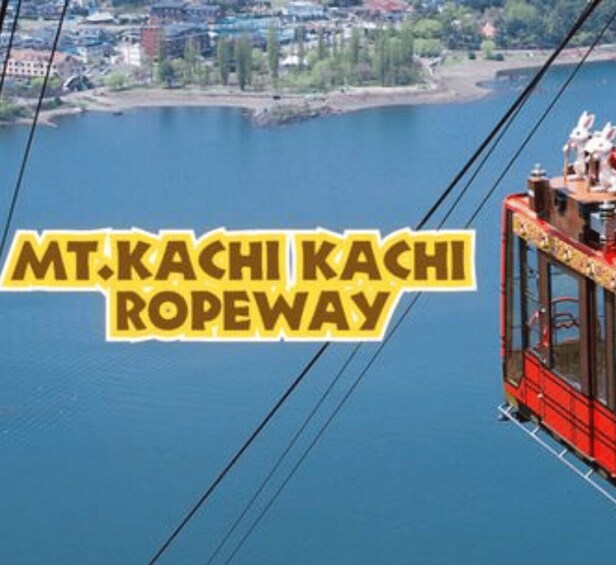A cable car with 'MT. KACHI KACHI ROPEWAY' text over a lake and town. 4