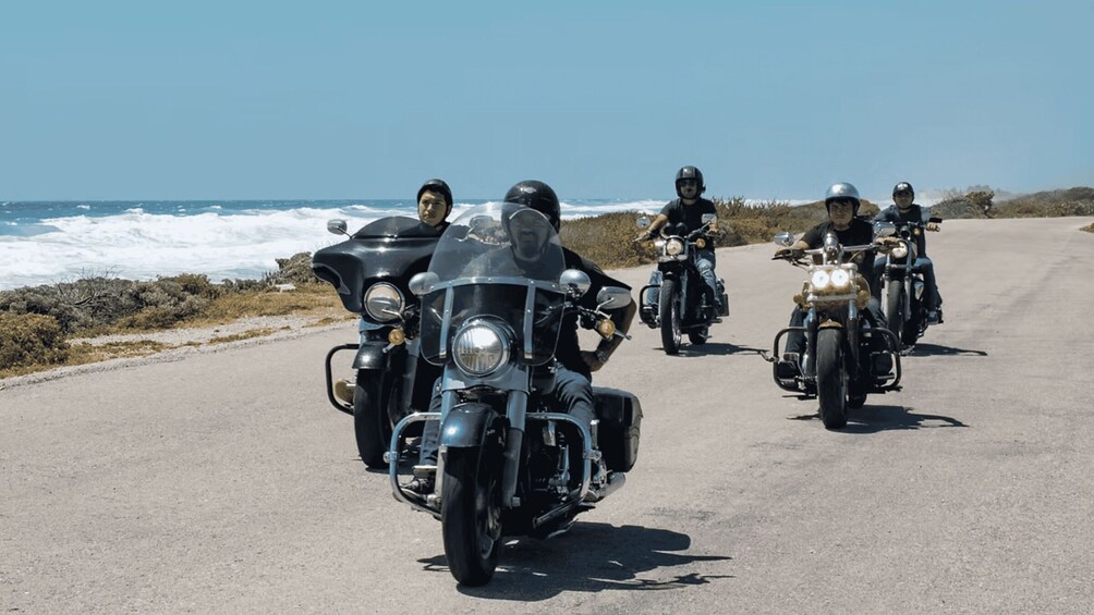 En grupp motorcyklister kör längs en kustväg med havet som bakgrund. 5
