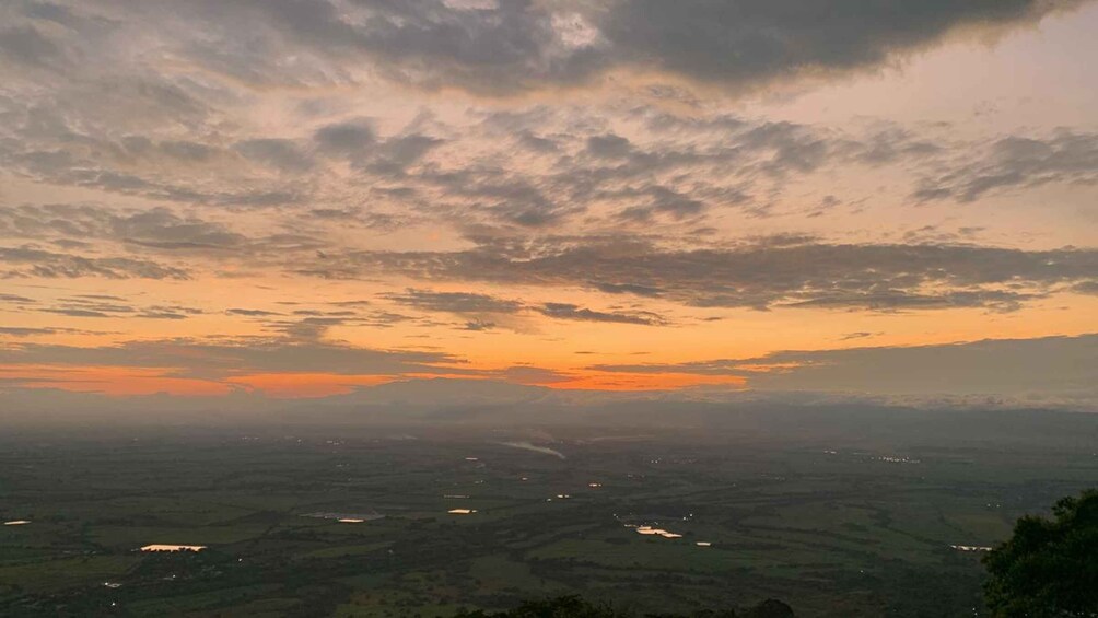 A landscape with a sunset, scattered clouds, and a valley with scattered lights. 1