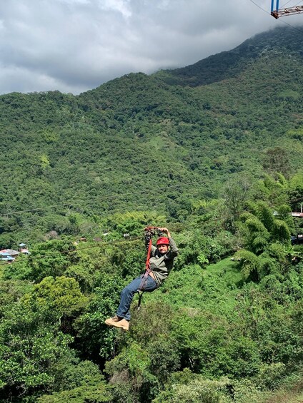 A person zip-lining through a forested area with mountains in the background. 3