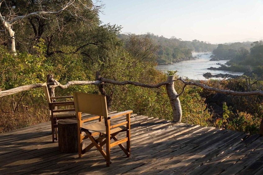 A wooden deck with a single chair overlooking a river and forested landscape. 5