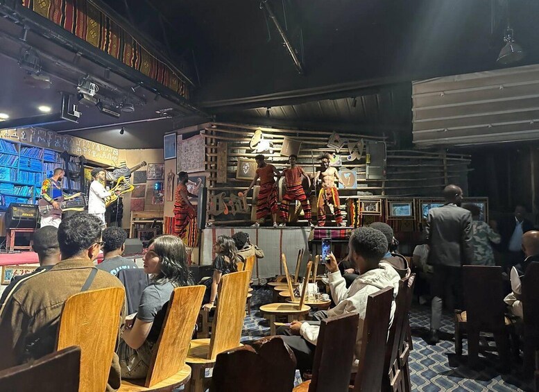 A restaurant with wooden chairs and tables, a stage with musicians, and a crowd of diners. 3