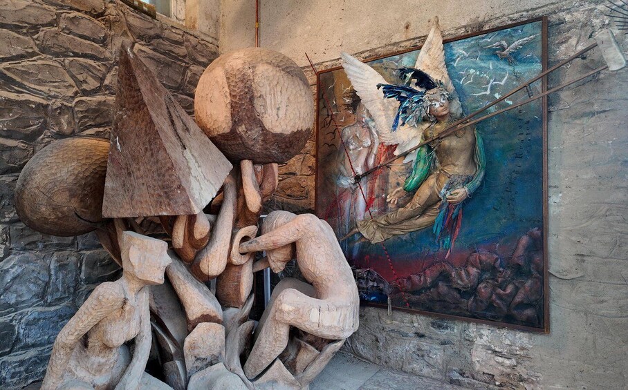 A sculpture of a human figure with a bird, a large wooden sphere, and a painting of a figure with wings. 4