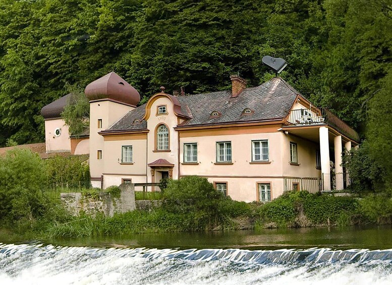 A large, multi-story house with a distinctive tower, situated by a river with a waterfall. 1