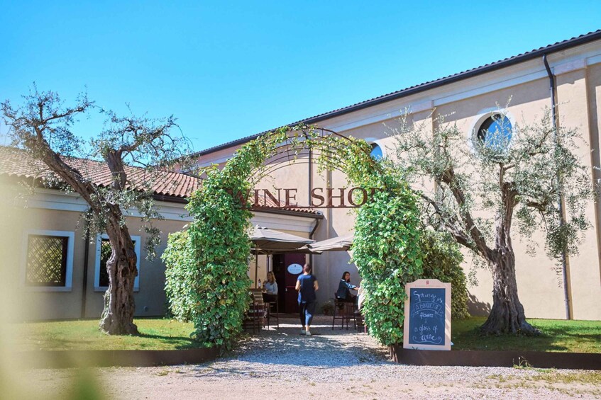 A wine shop with an archway of climbing vines, a gravel path, and a sign offering a glass of wine for a dollar. 4