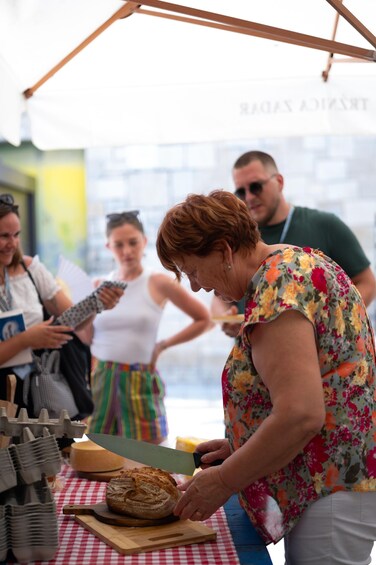 A person slicing bread on a wooden board at an outdoor event. 3