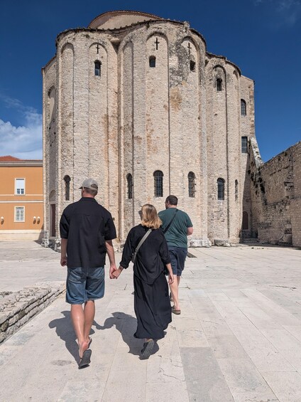 A group of people walking towards a historic stone building with arched windows and a cross on top. 5