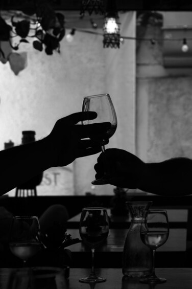 A person holding a wine glass, with other glasses and a pitcher on a table. 2