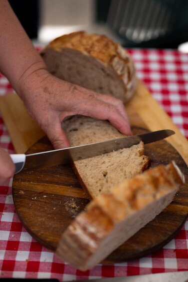 A person slicing a loaf of bread on a wooden cutting board. 4
