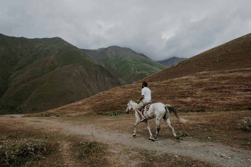 A person riding a horse on a dirt path in a hilly landscape. 1