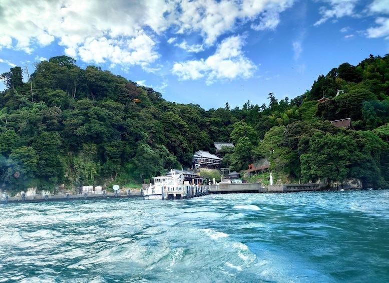 A coastal scene with a pier extending into the water, surrounded by lush green hills and a clear blue sky. 1