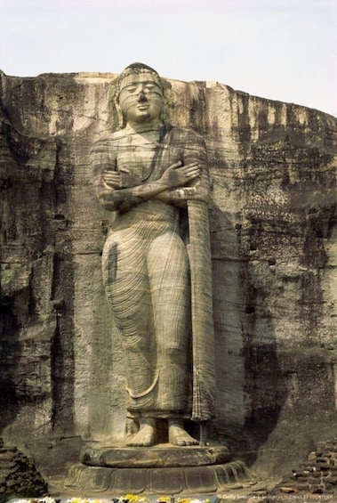 A large stone statue of a seated figure with crossed arms, set against a rocky cliff. 4