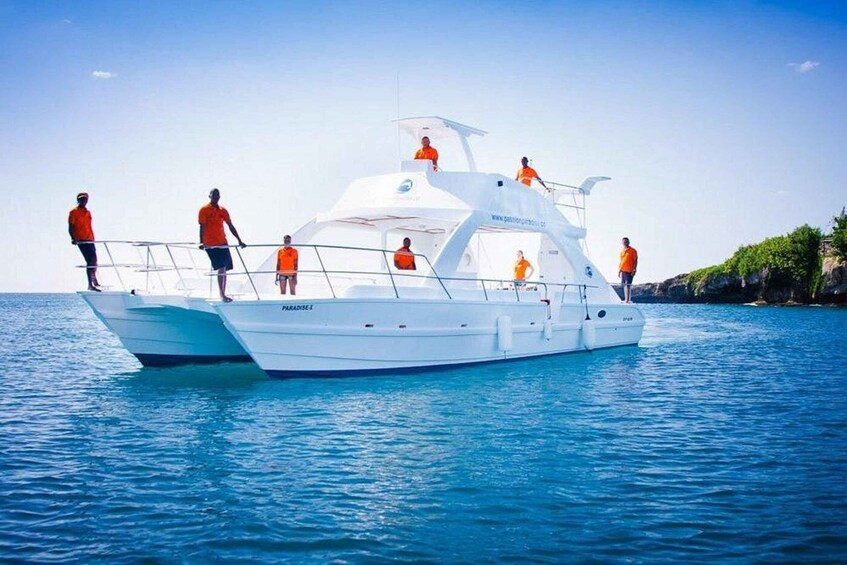 A white boat named 'Paradise' with people in orange shirts on board, sailing on clear blue water. 2