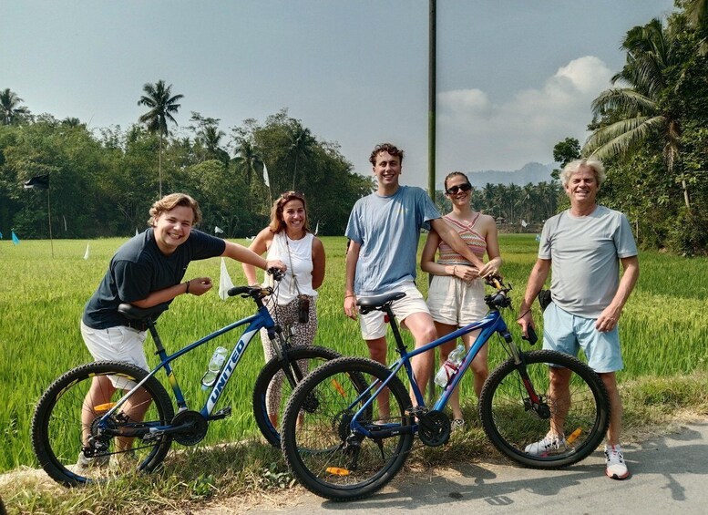 A group of people with bicycles in a rural setting with green fields and palm trees. 3