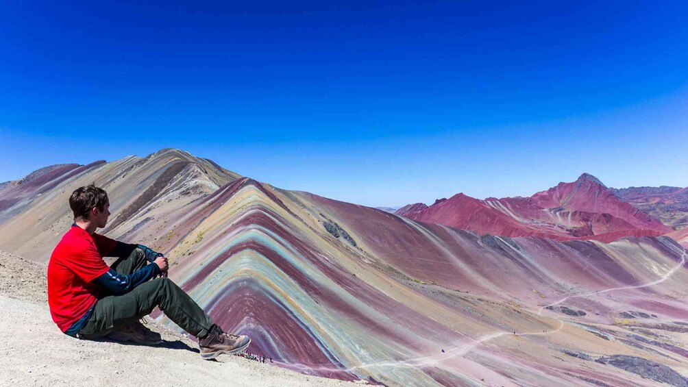 A person sitting on a mountain ridge with colorful rock formations in the background. 3