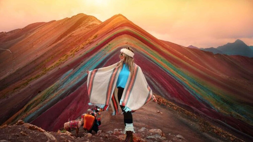 A person standing on a mountain with a colorful, layered rock formation in the background. 1