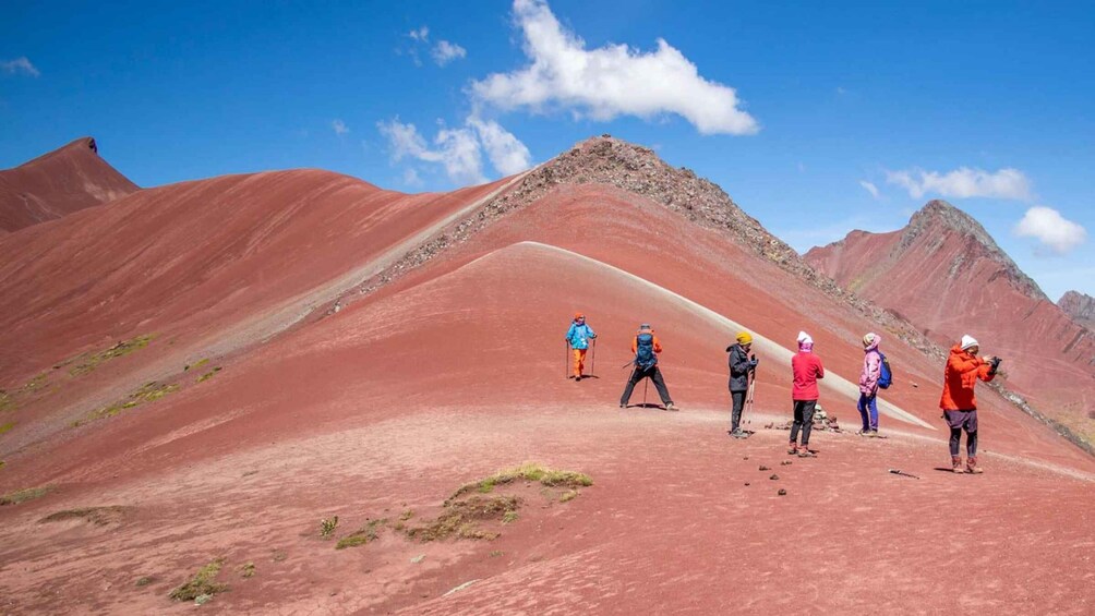 A group of hikers on a red-hued mountain trail with clear skies. 2