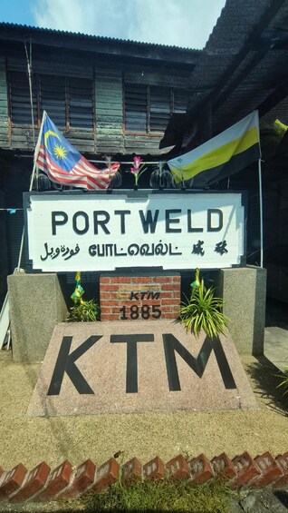 A sign for Port Weld with Malaysian and English text, a Malaysian flag, and a KTM logo with the year 1885. 1